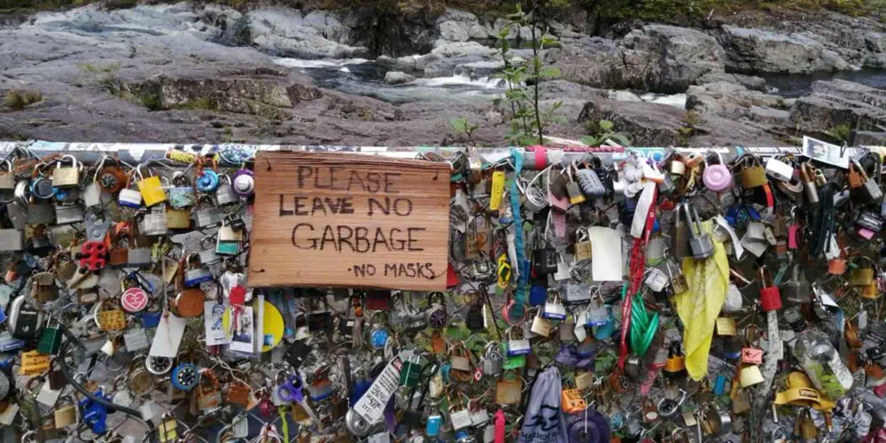 A chainlink fence along Highway 4 is covered with locks and garbage. It has a sign that says "please leave no garbage".