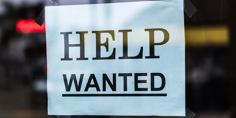 A "Help wanted" sign is taped inside a restaurant window.
