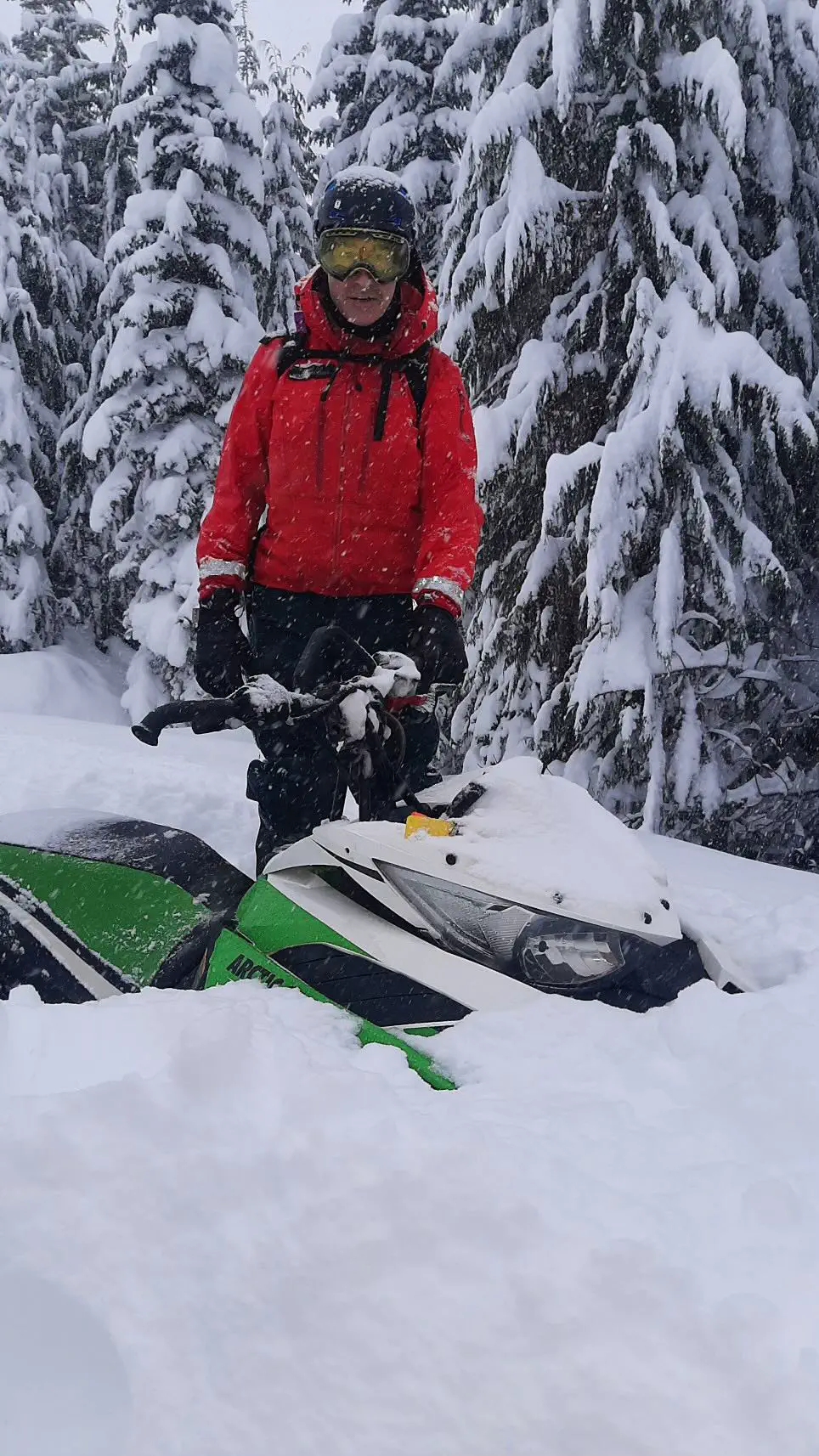 A member of the Comox Valley SAR stands with a snowmobile. It is nearly buried in snow.