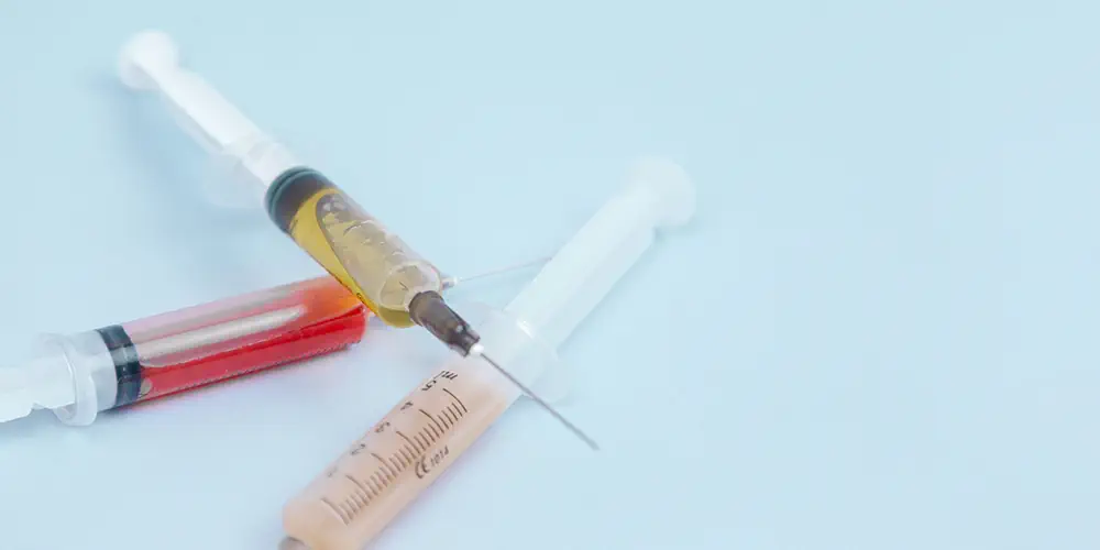 Three syringes full of liquid sit on a pale blue table.