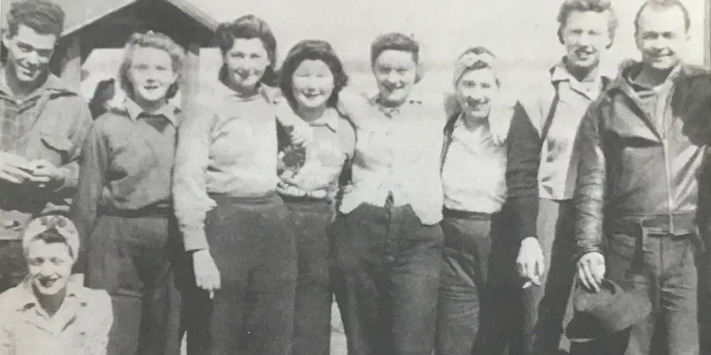 A black-and-white photo of the Plywood Girls standing in a line for the camera on a sunny day.