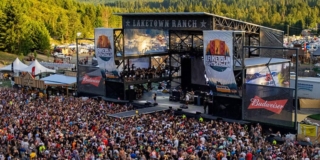 A huge crowd in front of an outdoor stage with green hills in the background.