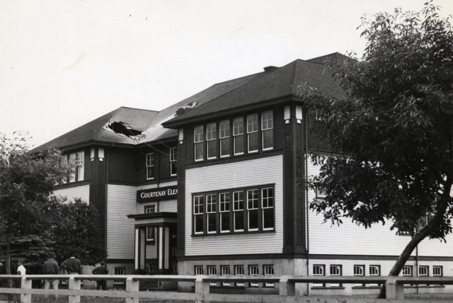 A black and white photo of the Courtenay Schoolhouse with a hole in the roof from earthquake damage.