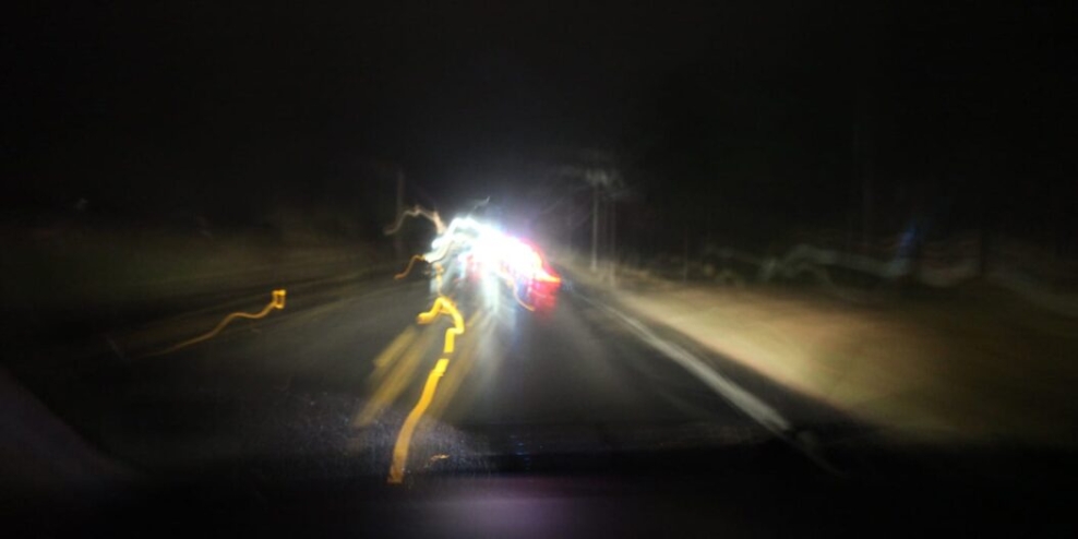 Streaky lights from a car swerve around the road at night.