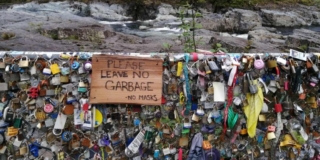 A chainlink fence along Highway 4 is covered with locks and garbage. It has a sign that says "please leave no garbage".
