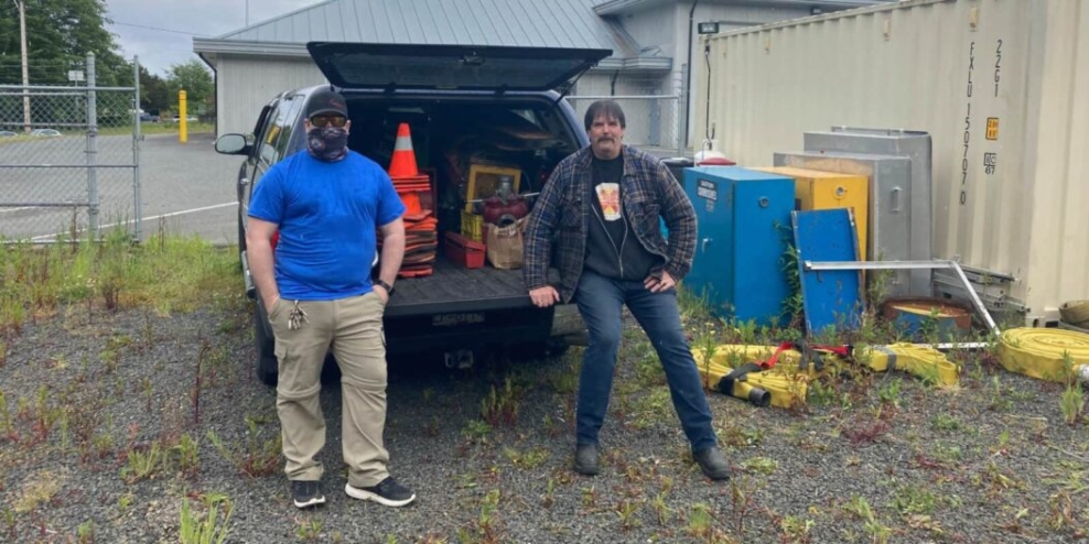 Two Port Hardy firefighters stand in front of a truck full of used fire fighting gear.