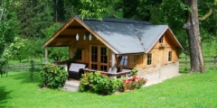 A small wooden house surrounded by trees. It has a large porch and slanted roof.