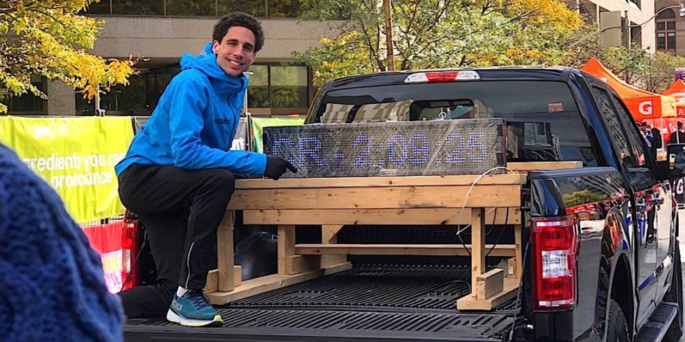 Cam Levins poses with a light display that reads his marathon time