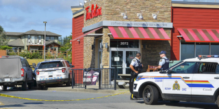 RCMP officers stand outside a Tim Horton's on a sunny day.