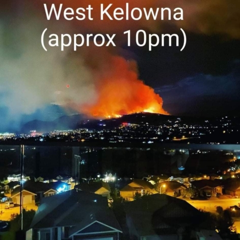 A nighttime picture of the West Kelowna fire burning near homes on a hill across a lake.