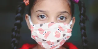 A small child with pigtails wearing a face mask with cartoon foxes on it.