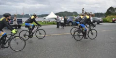 Cyclists ride off while people wave on a cloudy day.