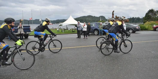 Cyclists ride off while people wave on a cloudy day.