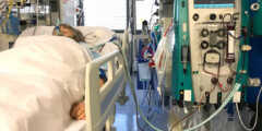 A woman lies in an ICU bed with wires and tubes hooked up to her body.