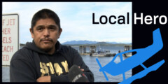 Kenny Brown in a black hooded sweater standing on the dock with water and mountains behind him.