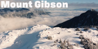 A drone shot from high above the top of Mount Gibson on a sunny day with whispy clouds. There are mountain peaks in the background.