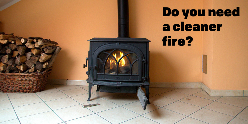 A wood stove sits against a peach coloured wall. There's a neat pile of firewood beside it.