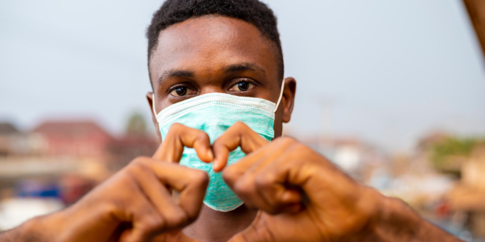 Young black man wearing a mask and making a heart with his hands.