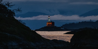 Fisgard lighthouse visible through steep hills with clouds and hills in background