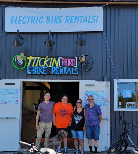 The family behind T̓iick̓in E-bike rentals poses outside their shop on a sunny day.