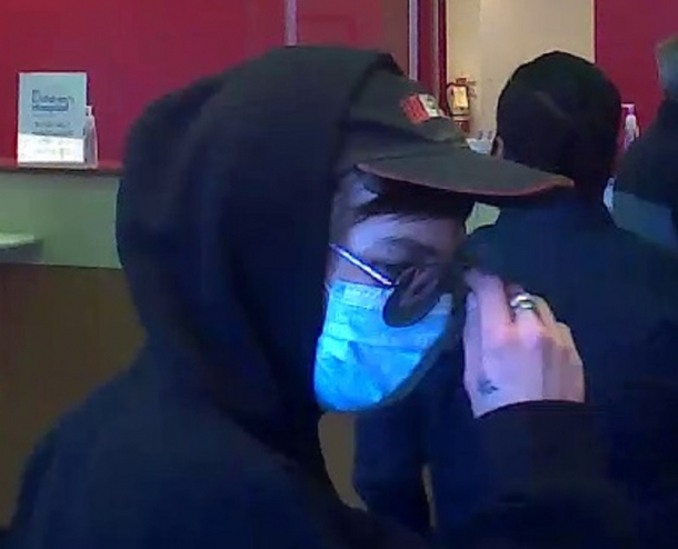 A closeup of a man with a hood, mask, and sunglasses taken from a security camera.