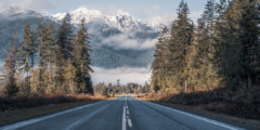 An empty two-lane highway stretches toward misty snowcapped mountains.