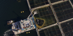 An aerial shot of a hydrolicer parked next to a floating factory fish farm.