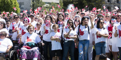 Folks gather outside the BC Legislature with Canadian flags on a sunny day.