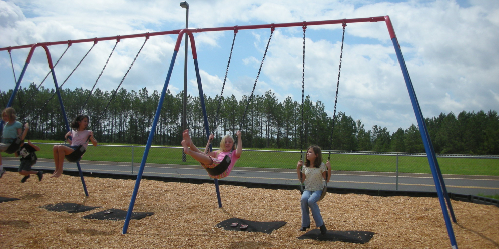 Girls play on a swingset on a sunny day.