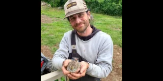 Justin Smith holds a baby rabbit in his hands while smiling at the camera. He's wearing an OK Tire cap.