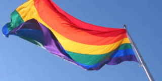 A rainbow flag flies on a sunny day.