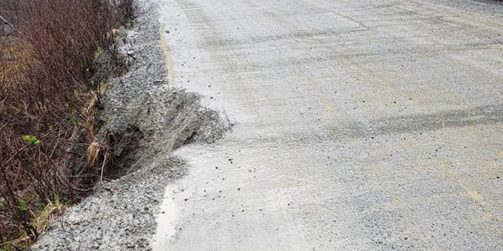 The edge of a gravel road crumbles into the bush below.