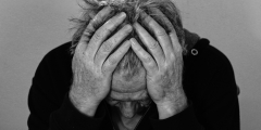 A black-and-white closeup of a man leaning forward with his head in his hands.