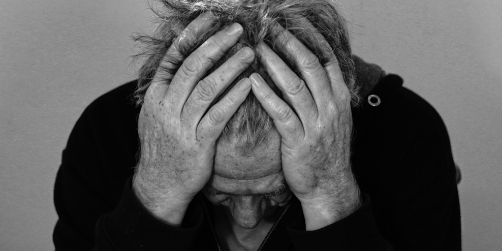 A black-and-white closeup of a man leaning forward with his head in his hands.