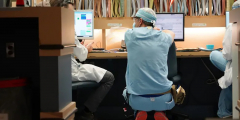 A tired healthcare worker crouches down between two doctors in front of a shelf full of files.