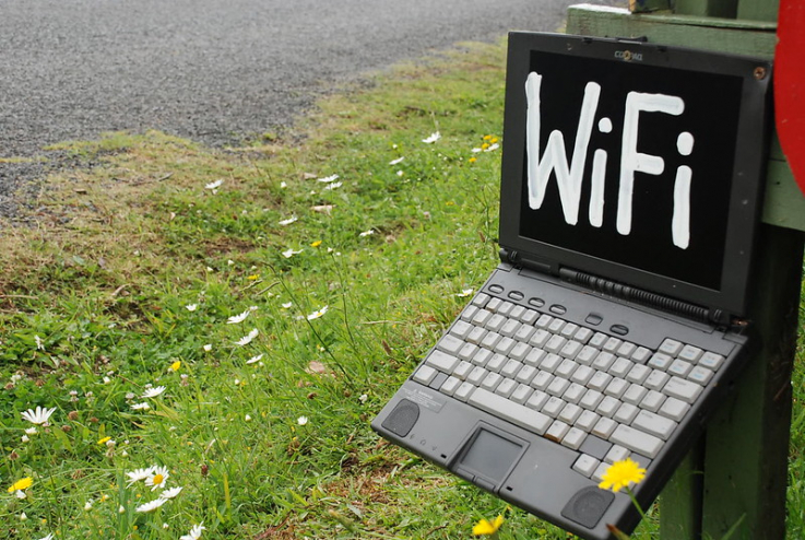 An old laptop is perched on a stoop outdoors. It has the word "WiFi" written on the screen in white paint.