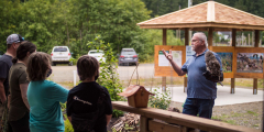 A handler talks to a group of kids while a raptor perches on his outstretched arm.