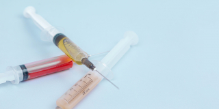 Three syringes full of liquid sit on a pale blue table.