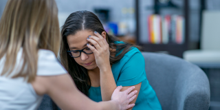 A woman comforts another woman in a clinical setting.