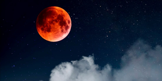 The blood moon on a dark night with clouds approaching.