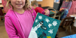 A young girl holds a bag decorated with a snowman and snowflakes for Christmas.