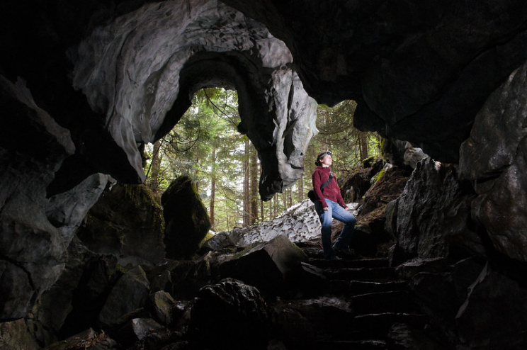 A woman wearing a head lamp stands in the archway of an undergound cave outside Gold River.