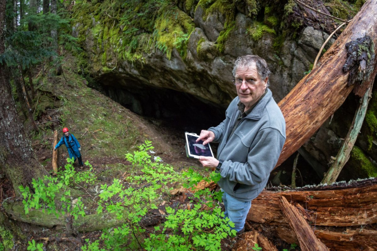 Paul Griffiths and Carol Ramsey stand inside a karst cave. Paul is holding an iPad, Carol is dressed in gear appropriate for going inside the caves.
