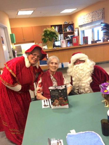 Folks dressed as Santa and Mrs Claus pose for a photo with a local senior.