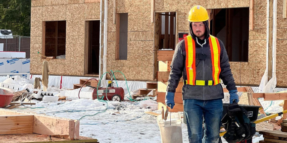 A construction worker moves materials around a build site in the snow.