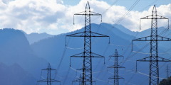 High tension power lines run between towers in front of a mountain landscape.